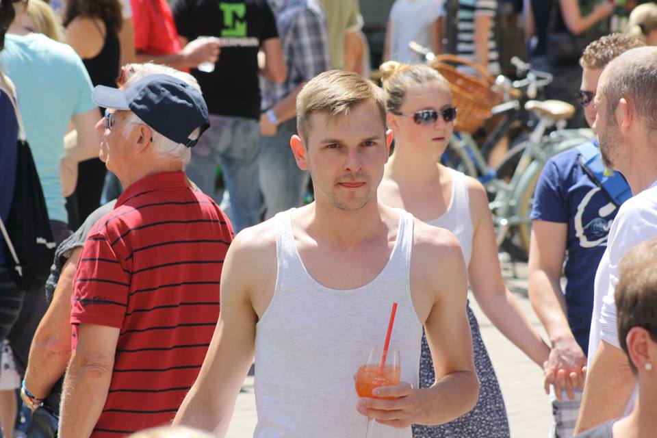 Ein junger Mann in einem weißen Tanktop hält ein Getränk in der Hand, während er sich auf einer belebten Straße