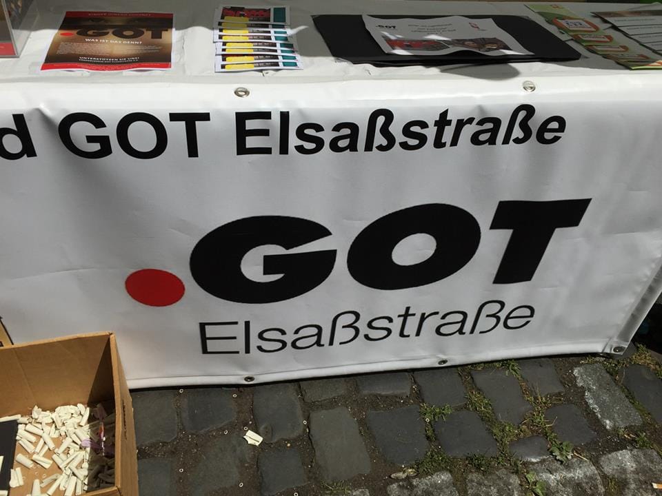 Ein Tisch mit einem Banner von GOT Elsassstraße, das in großen schwarzen Buchstaben und einem roten Punkt geschrieben ist, daneben