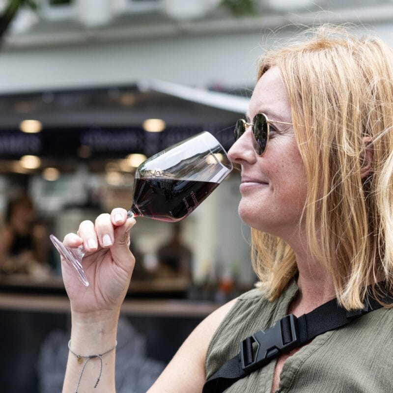 Eine Frau mit Sonnenbrille genießt ein Glas Rotwein und riecht am Glas auf einem Event.