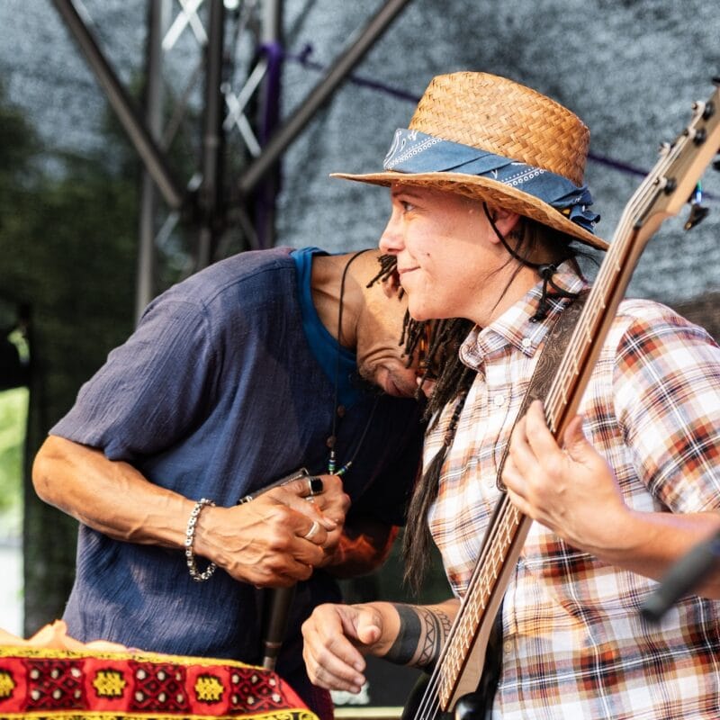 Zwei Musiker auf einer Bühne, einer mit Gitarre und Hut, der andere mit Dreadlocks.