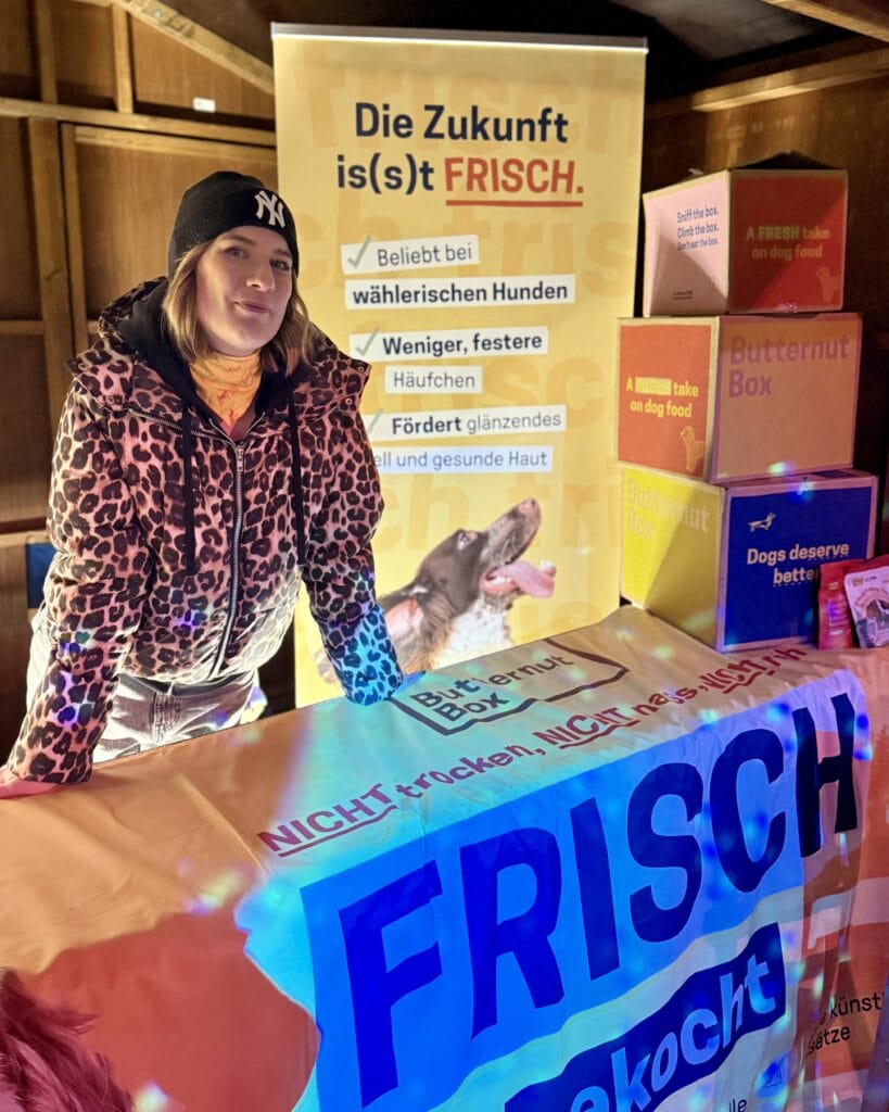 Eine Verkäuferin mit Mütze präsentiert einen Stand mit Hundefutter der Marke Butternut Box.