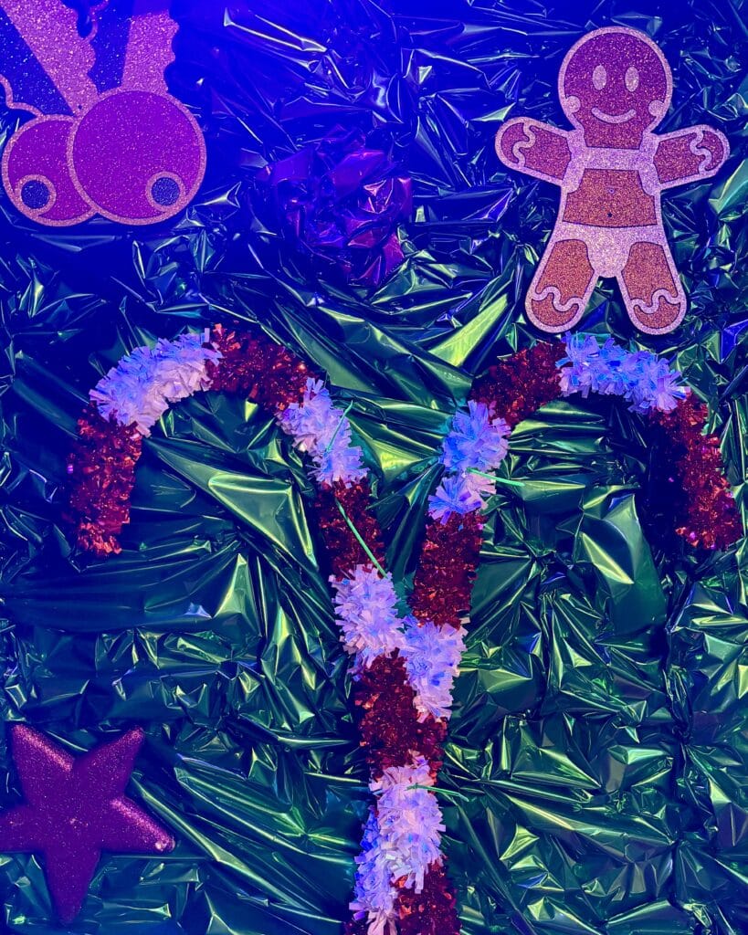 Auf einem glänzenden, grünen Hintergrund sind eine Zuckerstange, ein Lebkuchenmann, eine Stern und Weihnachtskugeln dekorativ angeordnet.