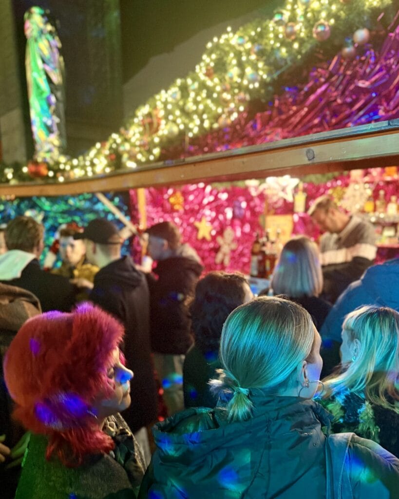 Auf einem Weihnachtsmarkt stehen Besucher vor einem Stand mit Weihnachtsdekoration und genießen die festliche Atmosphäre.