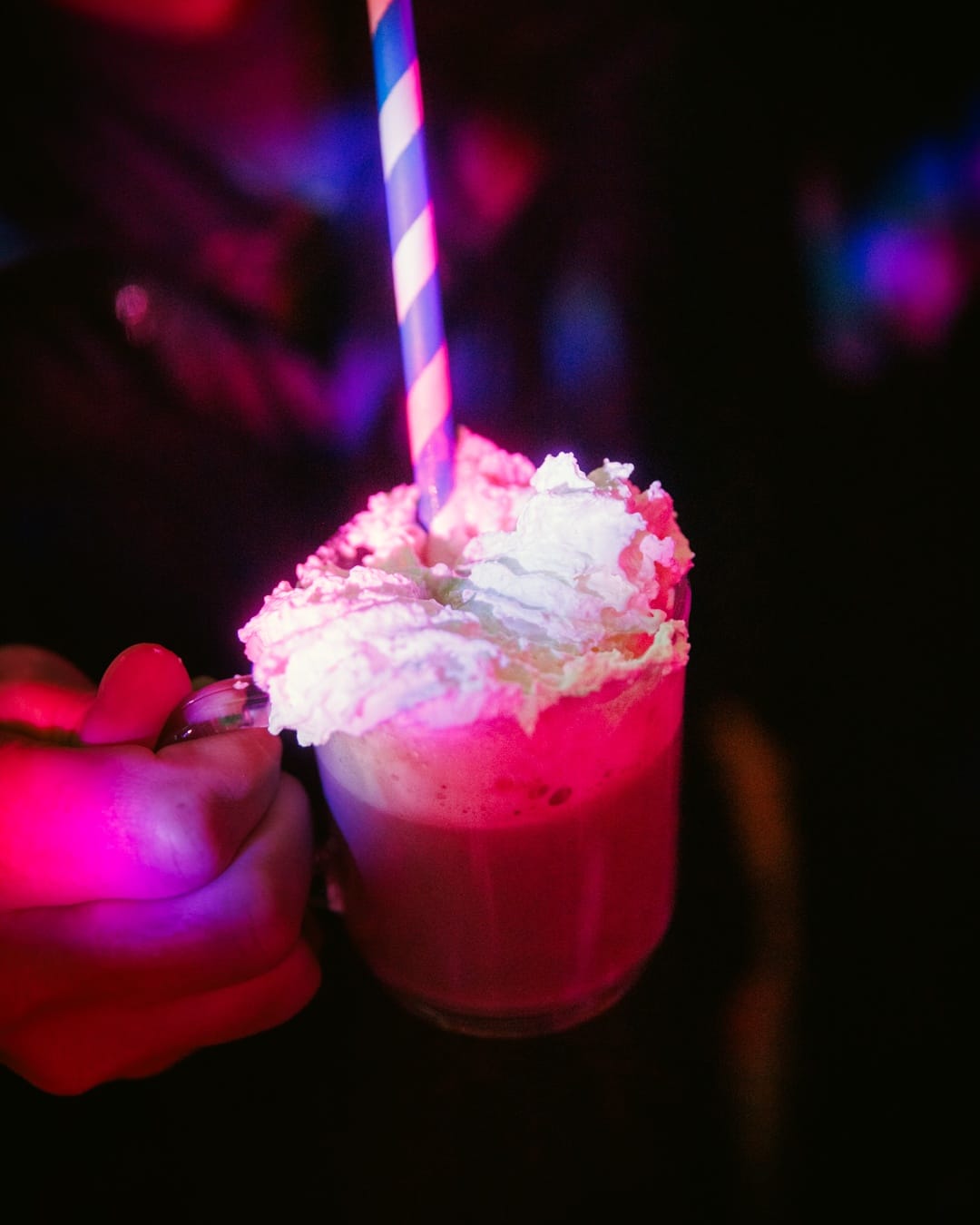 Auf einem Weihnachtsmarkt wird ein Heißgetränk mit Sahne und einem blau-weiß gestreiften Strohhalm in der Hand gehalten.