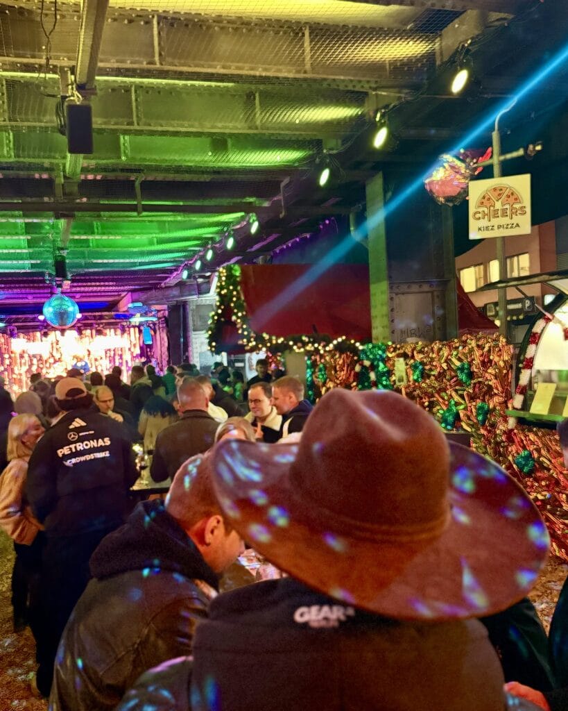 Besucher genießen die festliche Atmosphäre auf einem Event, buntes Licht erhellt die Szene und reflektiert auf Hüten.