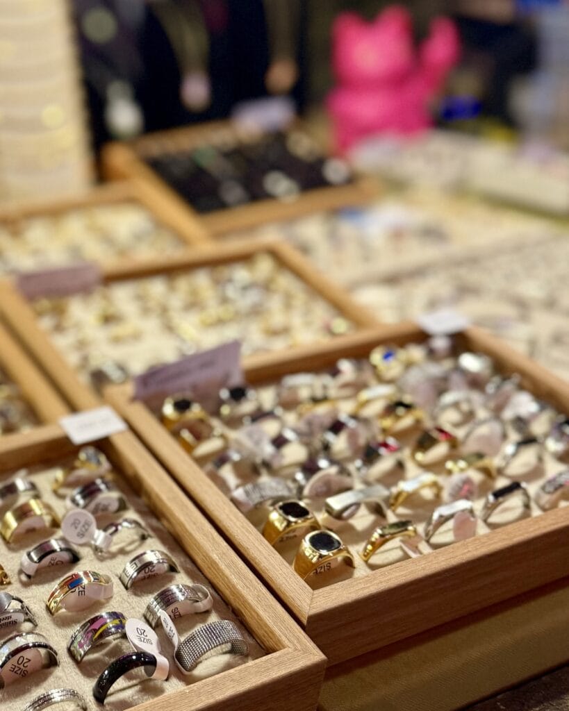 Auf einem Tisch präsentiert ein Verkäufer diverse Ringe in Holzrahmen mit verschiedenen Größen auf einem Markt.