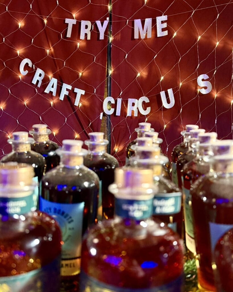 Viele Likörflaschen mit Korken stehen vor einer Wand mit Lichterketten und "Craft Circus" Schriftzug.