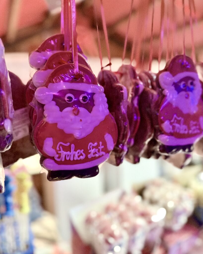 Aufgereihte Lebkuchen-Weihnachtsmänner mit Zuckerguss und der Aufschrift 'Frohes Fest' hängen an Bändern auf einem Weihnachtsmarkt.
