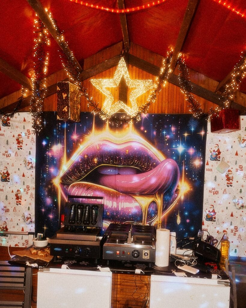 Ein weihnachtlich geschmückter Marktstand mit einem großen Lippen-Bild, Waffeleisen und festlicher Beleuchtung sorgt für festliche Stimmung.