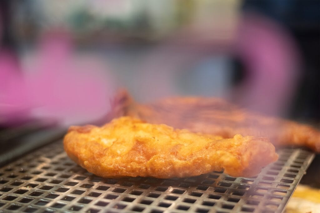 Ein Stück goldbraun frittierter Fisch liegt auf einem Metallrost und dampft, bereit zum Verzehr.