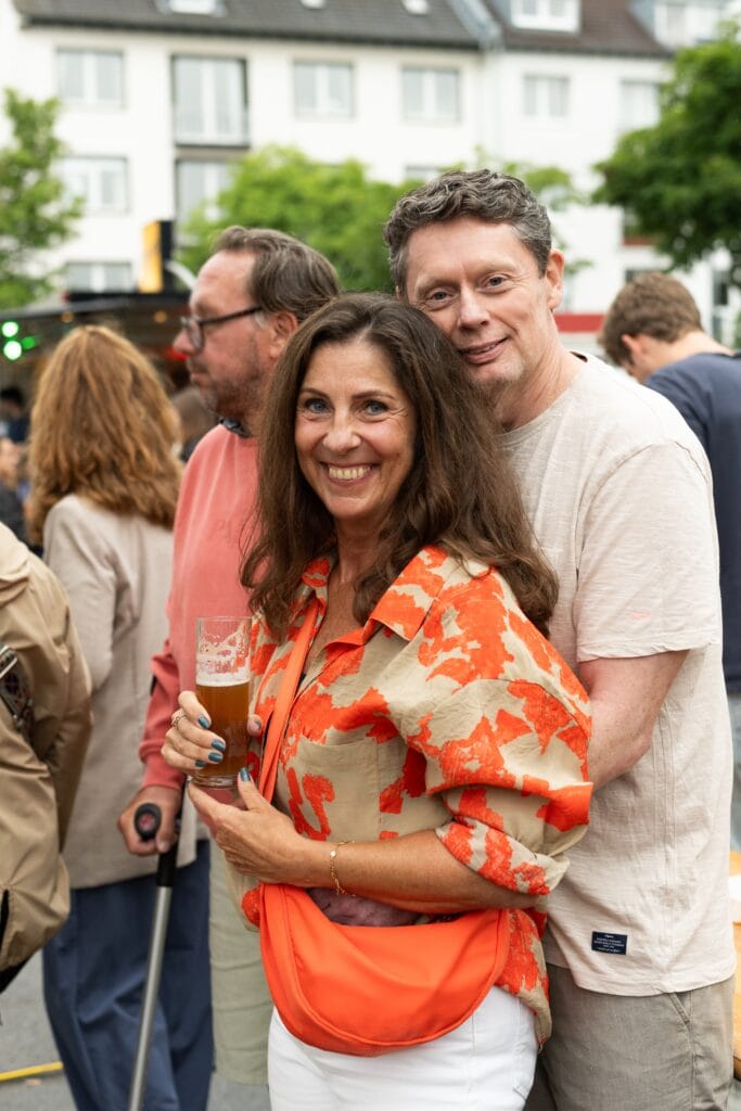 Ein lächelndes Paar mit einem Bierglas in der Hand posiert fröhlich auf einer Veranstaltung im Freien.