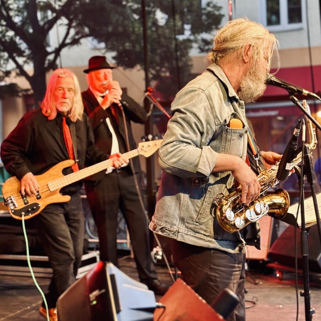 Eine Band spielt live auf der Bühne, mit Saxophon, Bass und Sänger in Anzügen.
