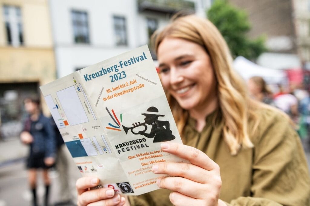 Eine junge Frau liest lächelnd einen Flyer für das Kreuzberg-Festival 2023 in Berlin, Kreuzberg.