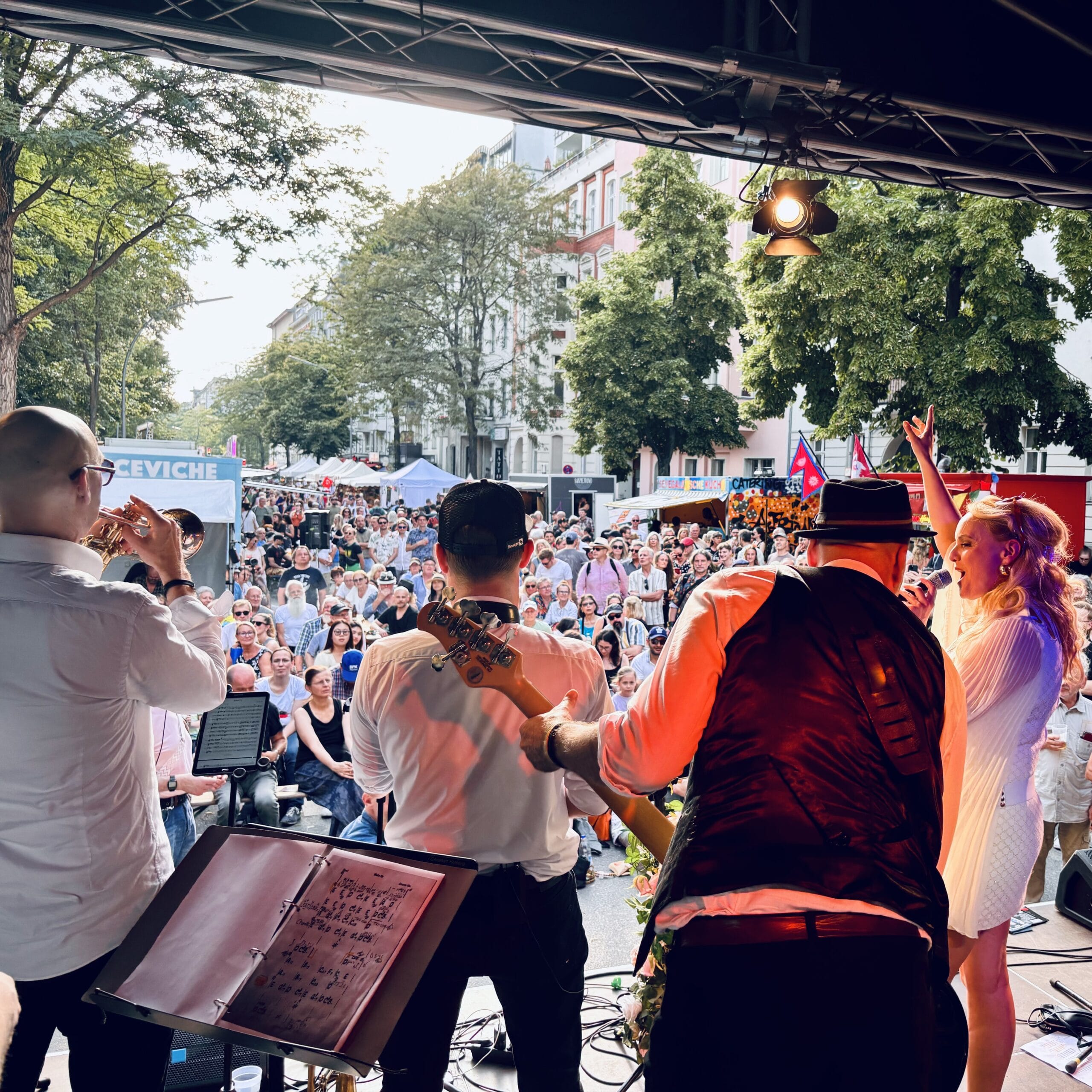 Eine Live-Band spielt auf einer Bühne vor einem großen Publikum im Freien, Sängerin und Musiker performen.