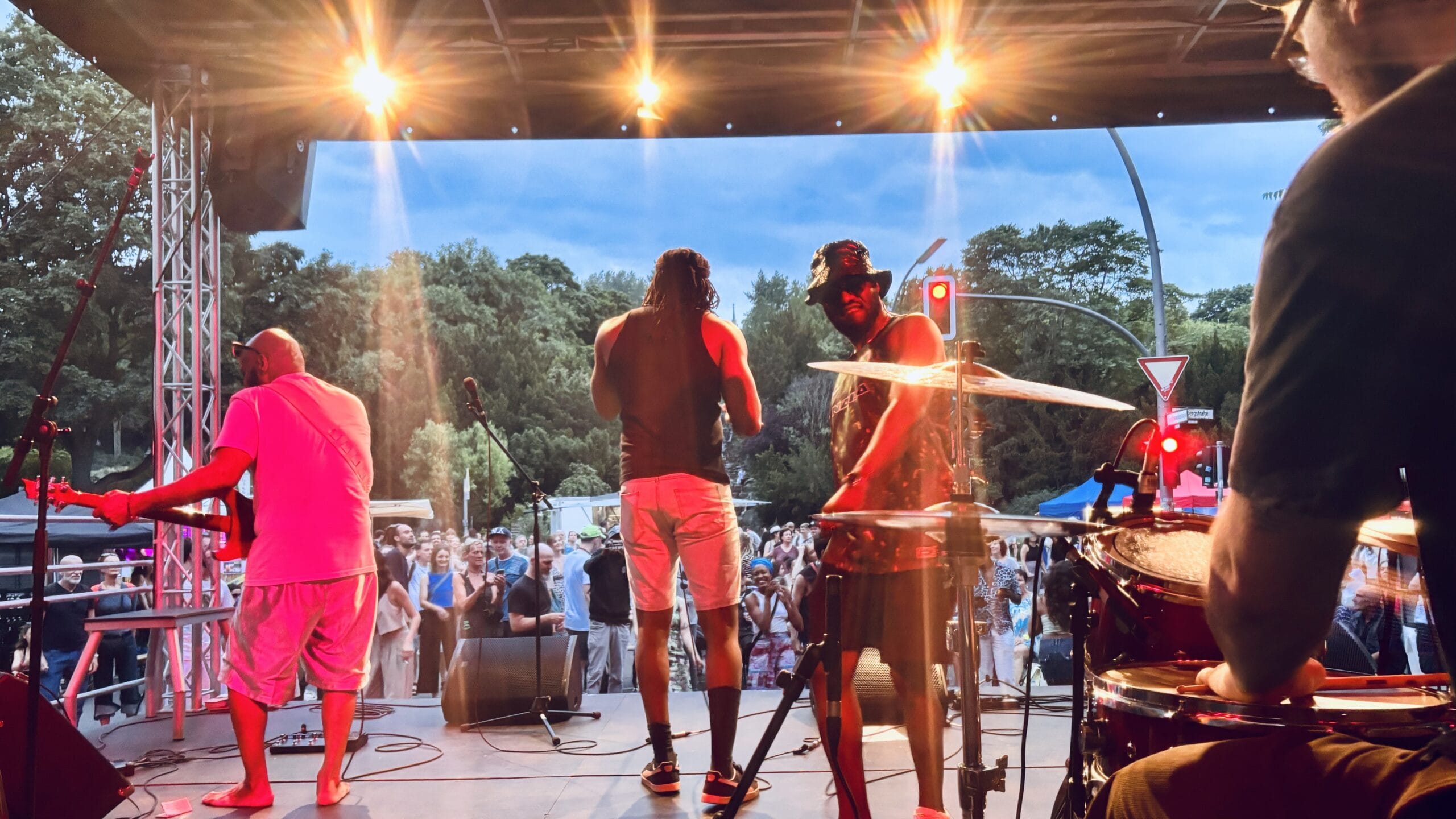 Eine Live-Band performt auf einer Bühne vor Publikum, mit Bäumen im Hintergrund und Bühnenbeleuchtung.