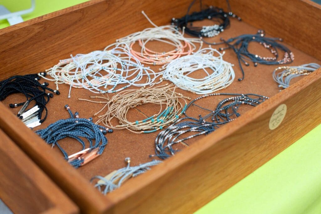 Eine Holzkiste präsentiert eine Auswahl an filigranen Armbändern in verschiedenen Farben und Designs, die zum Verkauf angeboten werden.