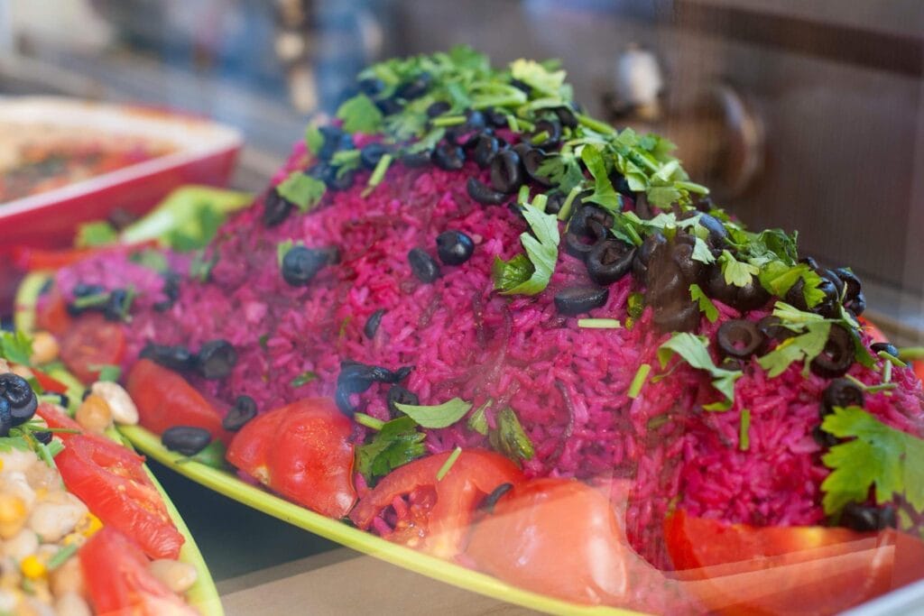 Ein appetitlicher Beet-Reis-Salat mit Tomaten, Oliven und frischen Kräutern wird auf einem gelben Teller präsentiert.