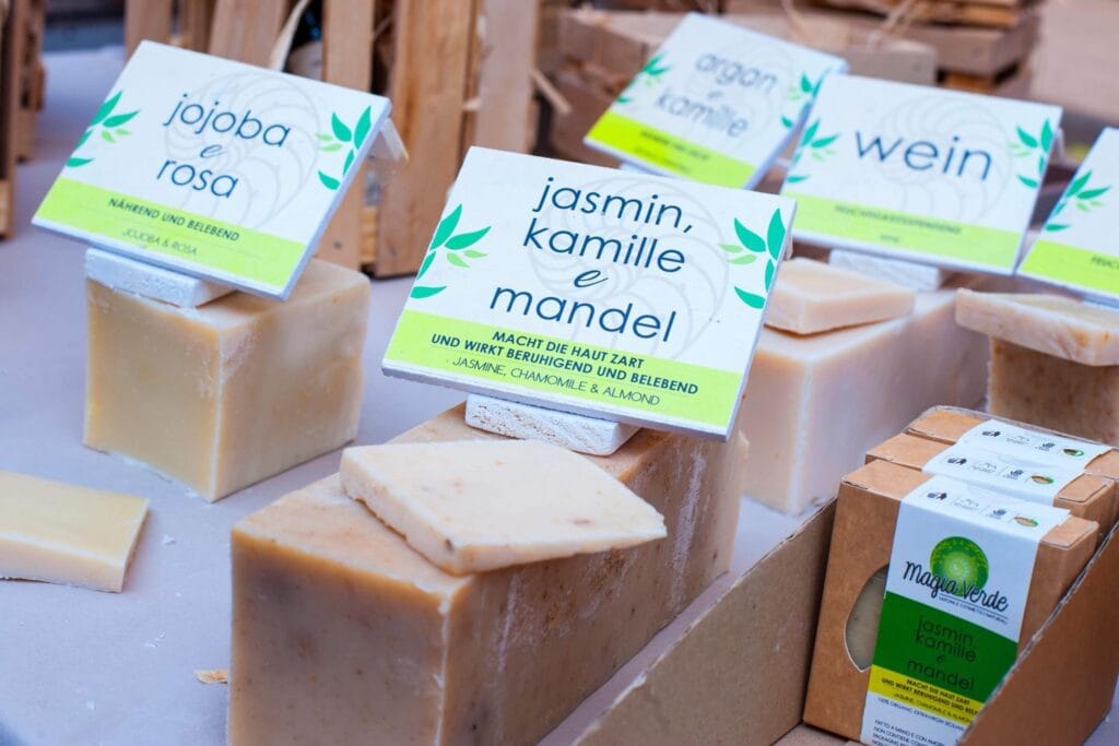 Verschiedene handgemachte Seifenstücke mit Kräuternamen und Beschreibungen werden auf einem Tisch zum Verkauf angeboten.