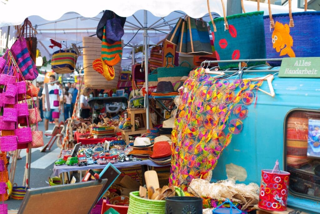 Ein bunter Marktstand präsentiert eine Vielfalt an handgefertigten Waren wie Taschen, Hüte und bunte Tücher für interessierte Käufer.