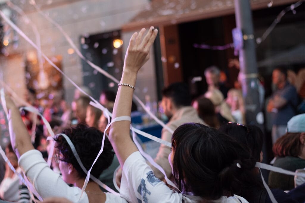 Zwei junge Frauen jubeln mit erhobenen Armen und Konfetti in der Luft, umgeben von weiteren Gästen.