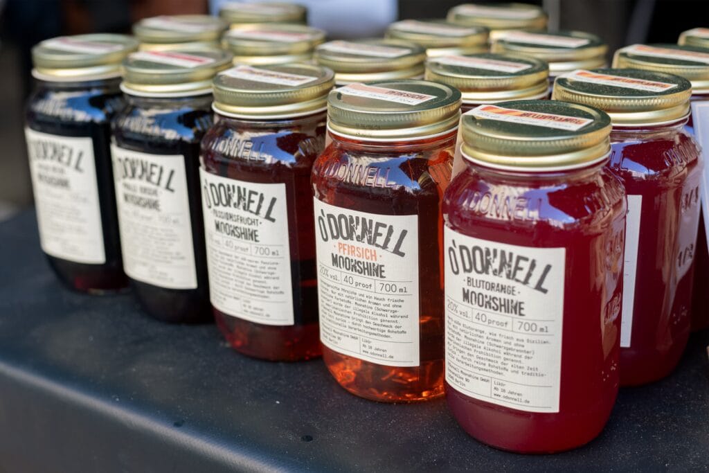 Viele Einmachgläser mit O'Donnell Moonshine in verschiedenen Geschmacksrichtungen stehen auf einem dunklen Tisch zum Verkauf.
