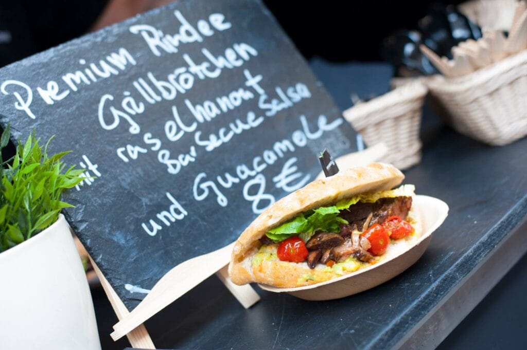 Ein appetitliches Premium Rindfleisch Grillbrötchen mit Salat und Tomaten liegt neben einer Tafel mit der Speisekarte.