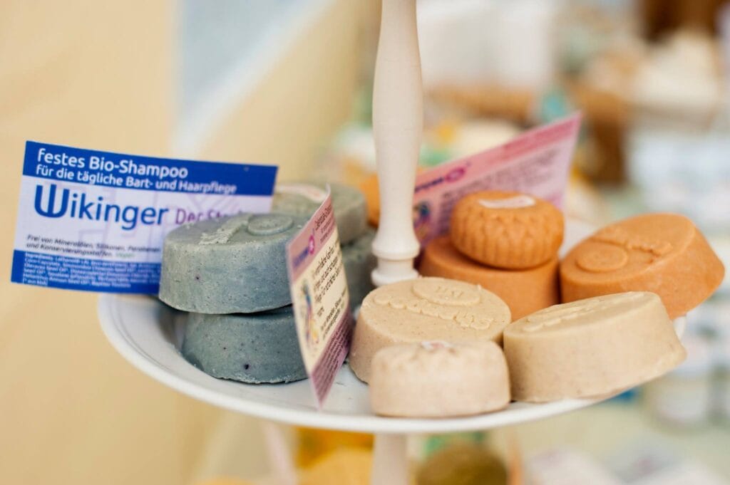 Auf einem Teller liegen verschiedenfarbige, feste Shampoo-Stücke mit kleinen Informationskarten, die Inhaltsstoffe und Marke zeigen.