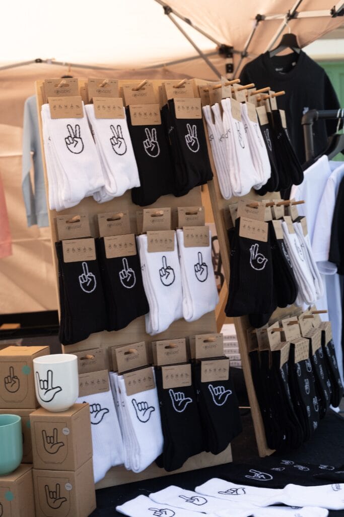 Auf einem Verkaufsstand werden Socken in Schwarz und Weiß mit verschiedenen Handmotiven präsentiert, dazu passende Tassen und T-Shirts.