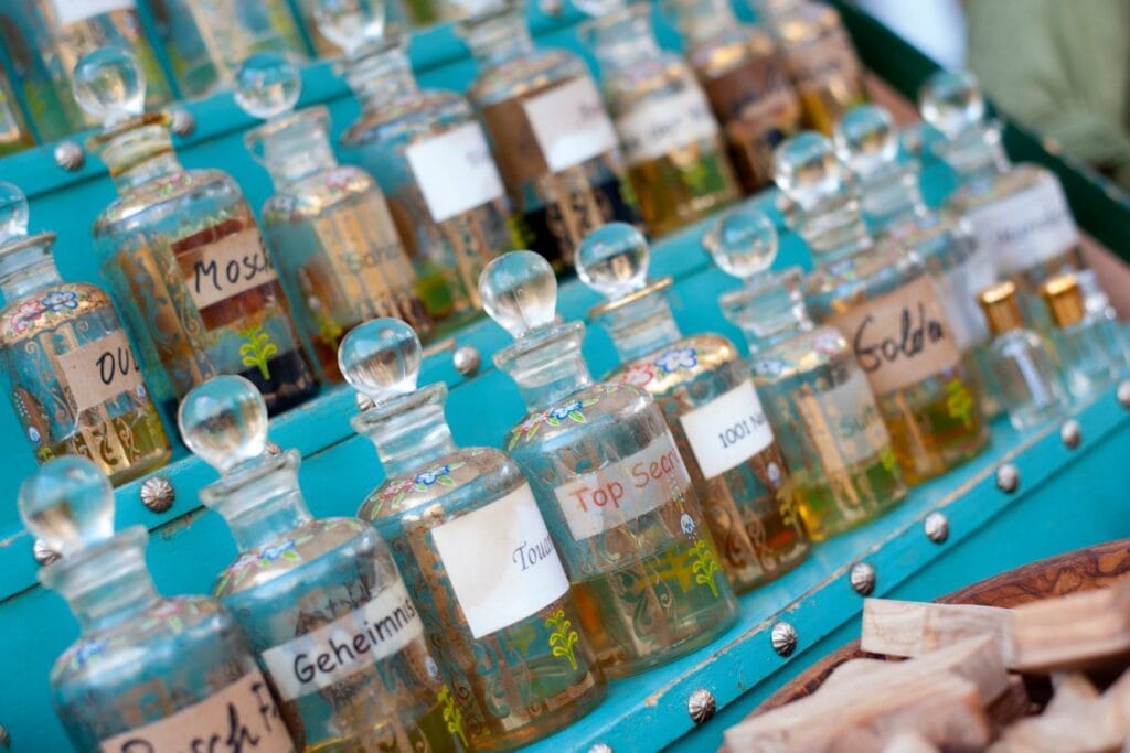 Viele kleine Parfümflaschen mit verschiedenen Aufschriften stehen auf einem dekorierten Regal, einige davon mit handgeschriebenen Etiketten.