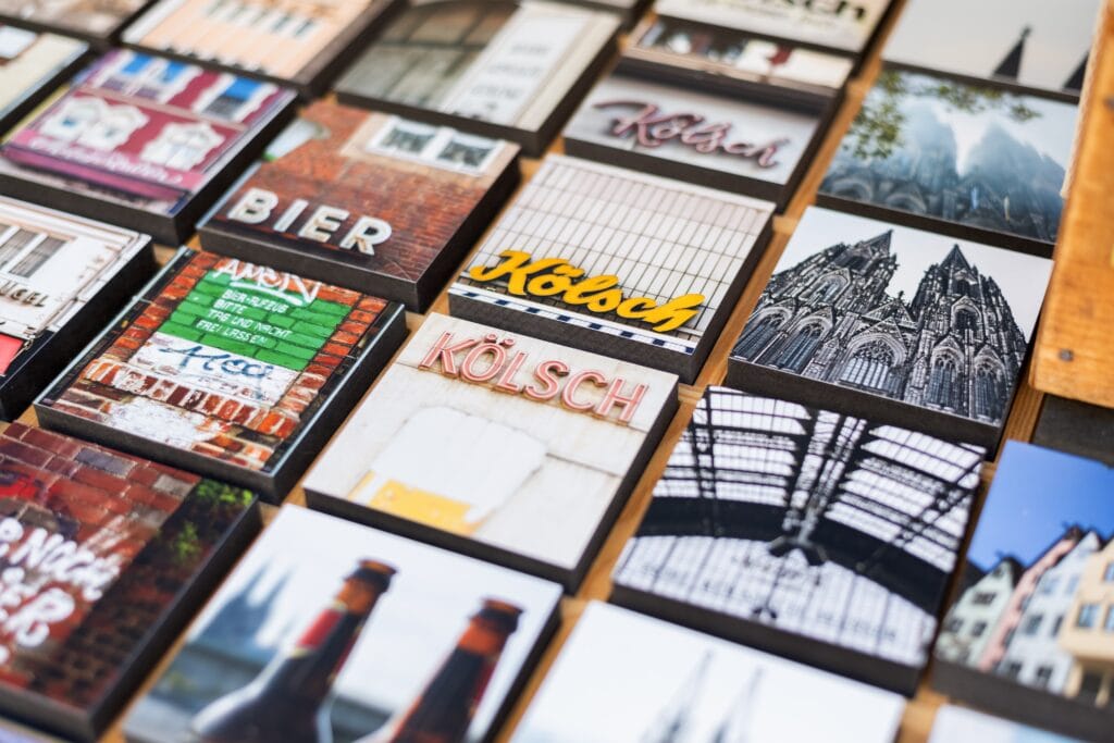 Viele kleine Köln-Souvenirs liegen auf einem Tisch, darunter Bilder vom Dom, Kölsch-Glas und typischen Brauhäusern.