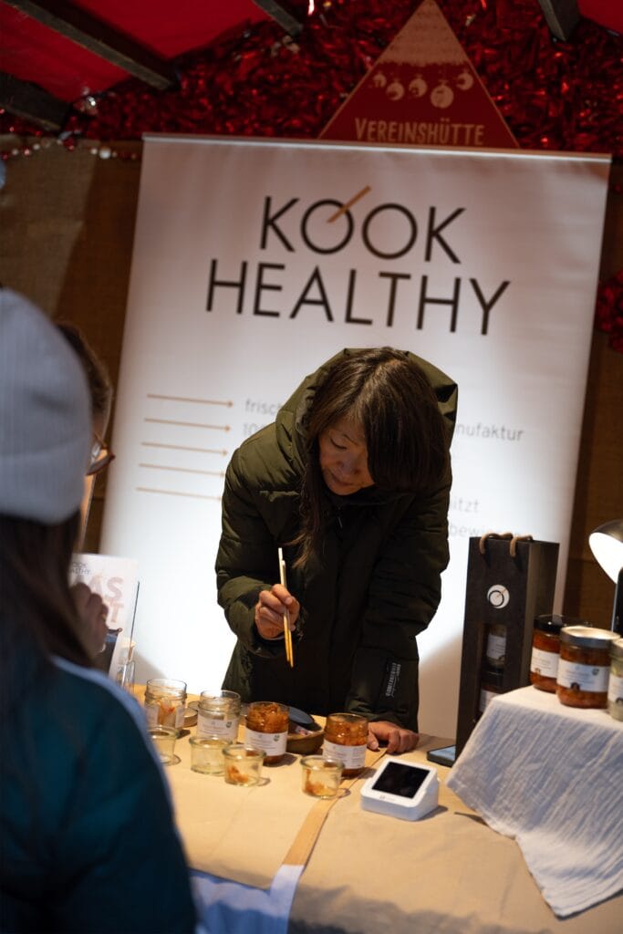 Eine Verkäuferin reicht einem Besucher eine Kostprobe von Produkten an einem liebevoll dekorierten Stand.
