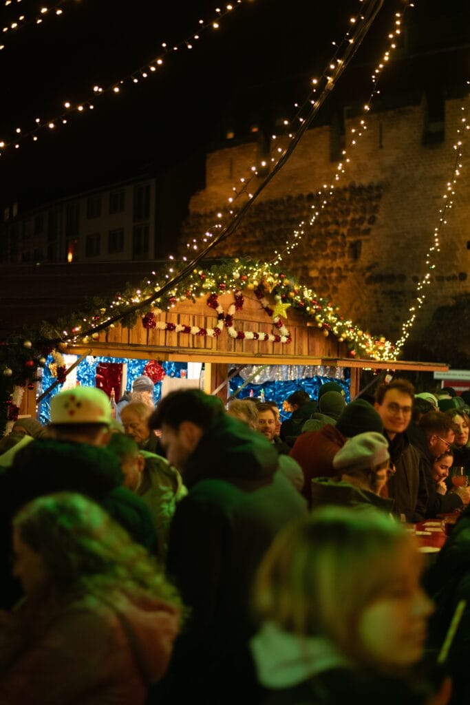 Aufnahme von Menschen, die sich vor einem Weihnachtsmarktstand auf dem Veedelsadvent in Köln versammeln.