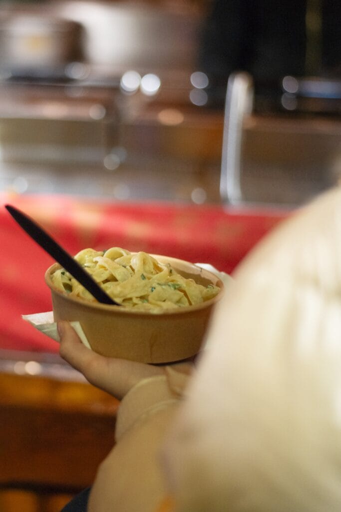 Eine Person hält eine Pappschale mit Pasta in der Hand, bereit, sie zu essen.