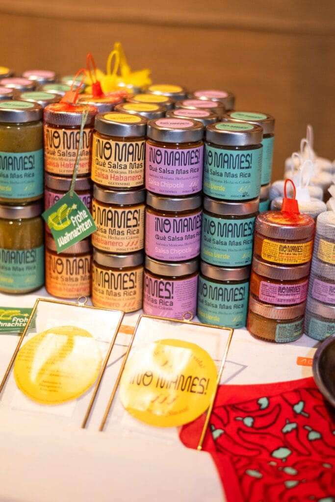 Verschiedene bunte Salsa-Gläser von No Mames! stehen auf einem Tisch zum Verkauf.