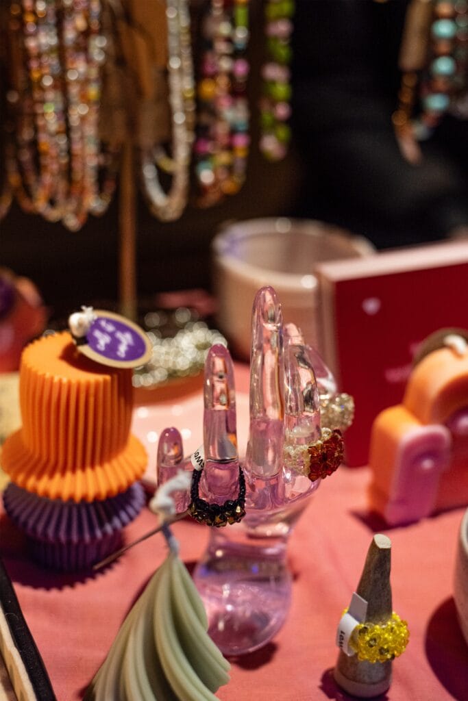Auf einem Marktstand werden bunte Schmuckstücke, darunter Ringe und Ketten, auf einer pinkfarbenen Oberfläche präsentiert.