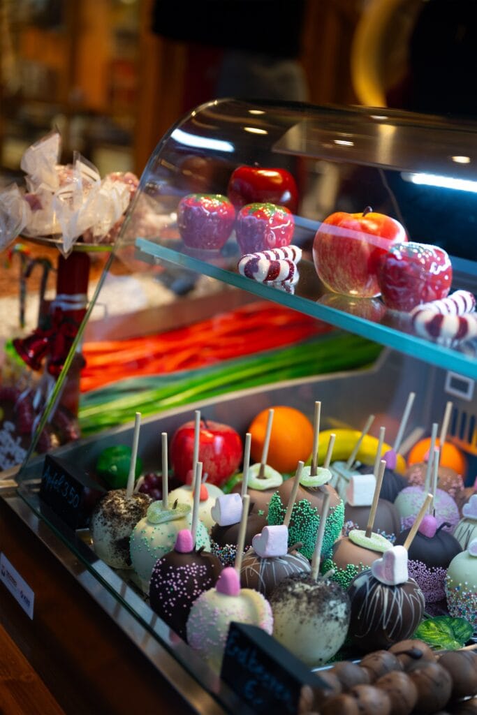 Ein buntes Schaufenster mit kandierten Äpfeln, Schokoriegeln und Marshmallows auf einem Weihnachtsmarkt voller süßer Köstlichkeiten.