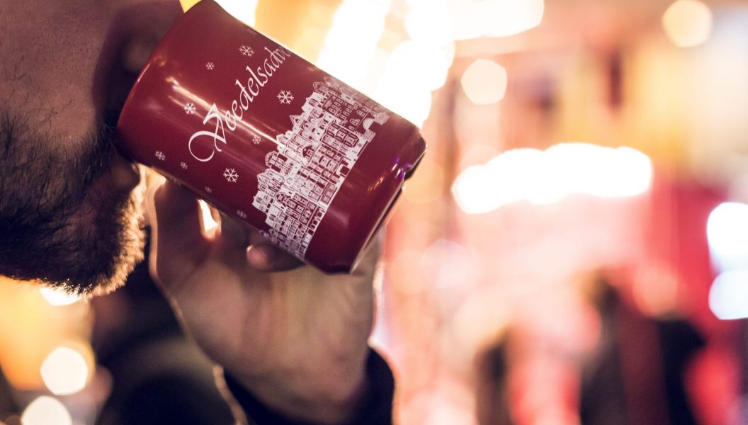 Person trinkt aus einer Weihnachtstasse mit der Aufschrift "Veedelsadvent" in Köln